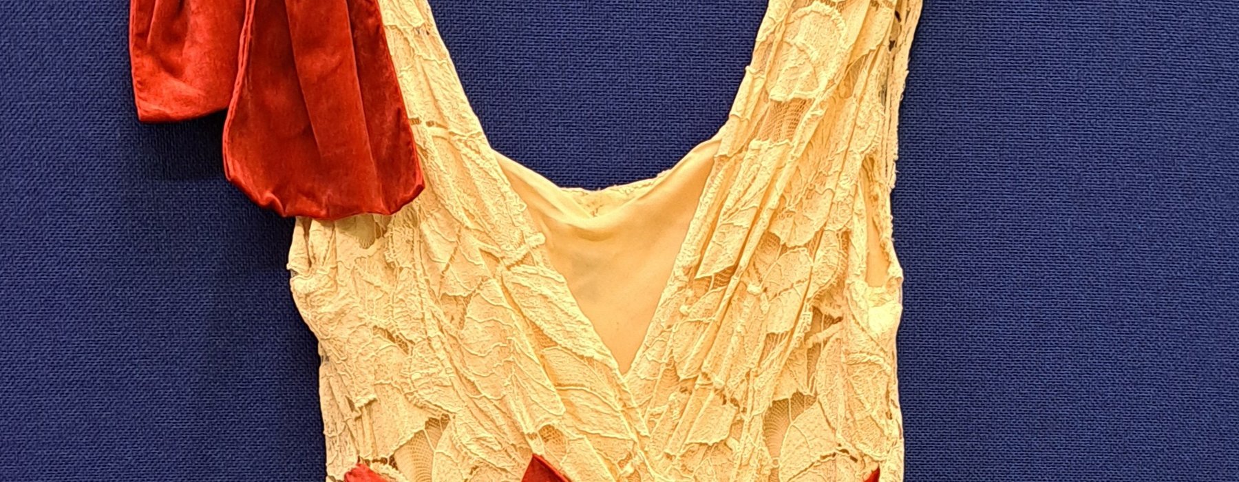 Long cream evening dress with red bow and red detail on the shoulder, on a hanger
