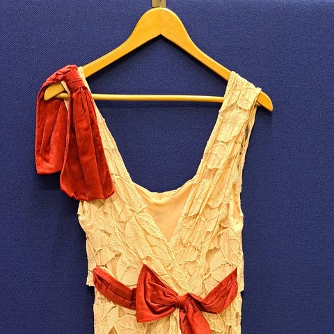 Long cream evening dress with red bow and red detail on the shoulder, on a hanger