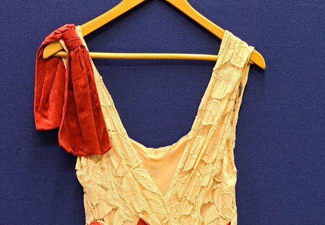Long cream evening dress with red bow and red detail on the shoulder, on a hanger