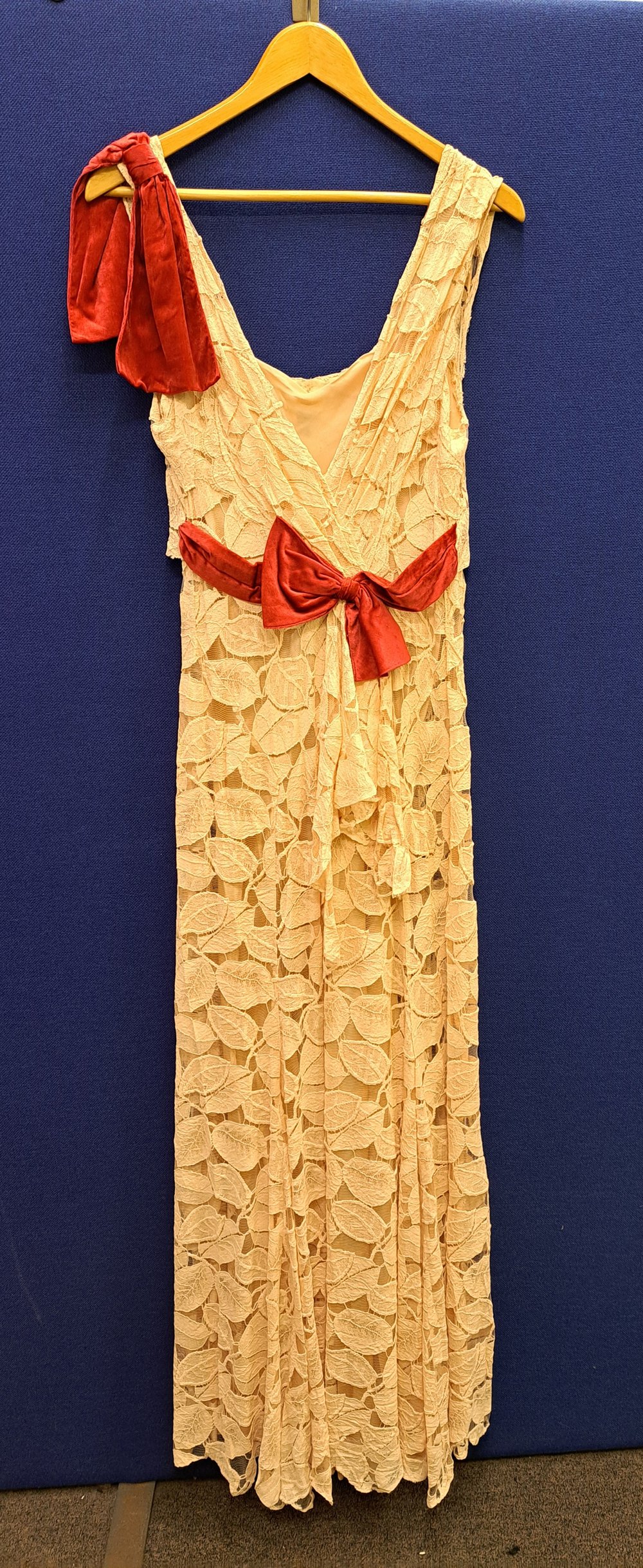 Long cream evening dress with red bow and red detail on the shoulder, on a hanger