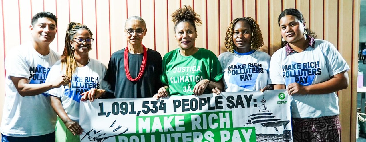 Activists and Brazil's Environment Minister standing in a line with a banner that says: '1,091,534 people say: Make rich polluters pay', at COP30 in Brazil.