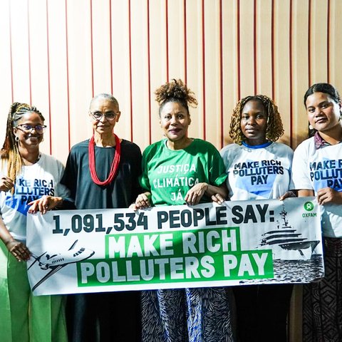 Activists and Brazil's Environment Minister standing in a line with a banner that says: '1,091,534 people say: Make rich polluters pay', at COP30 in Brazil.