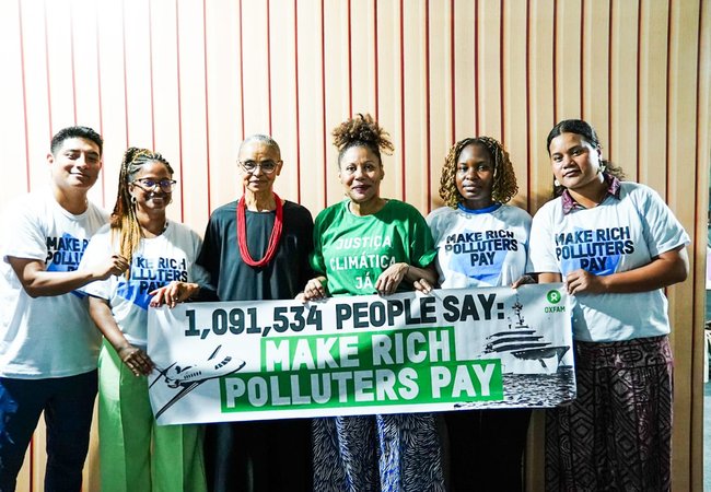Activists and Brazil's Environment Minister standing in a line with a banner that says: '1,091,534 people say: Make rich polluters pay', at COP30 in Brazil.