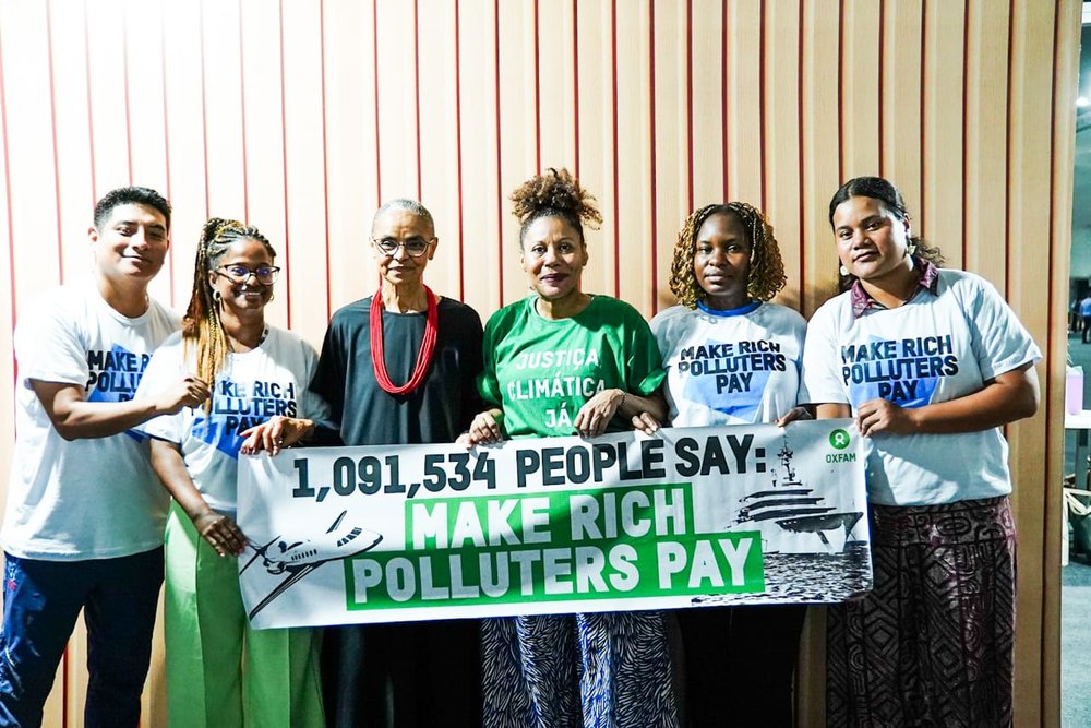 Activists and Brazil's Environment Minister standing in a line with a banner that says: '1,091,534 people say: Make rich polluters pay', at COP30 in Brazil.