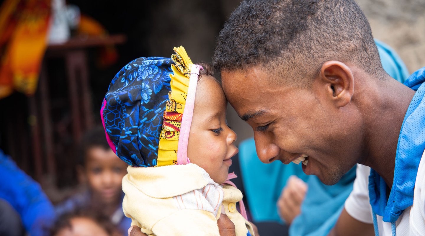 Munadhel holds his baby brother. His baby brother is wearing a blue and yellow bonnet.