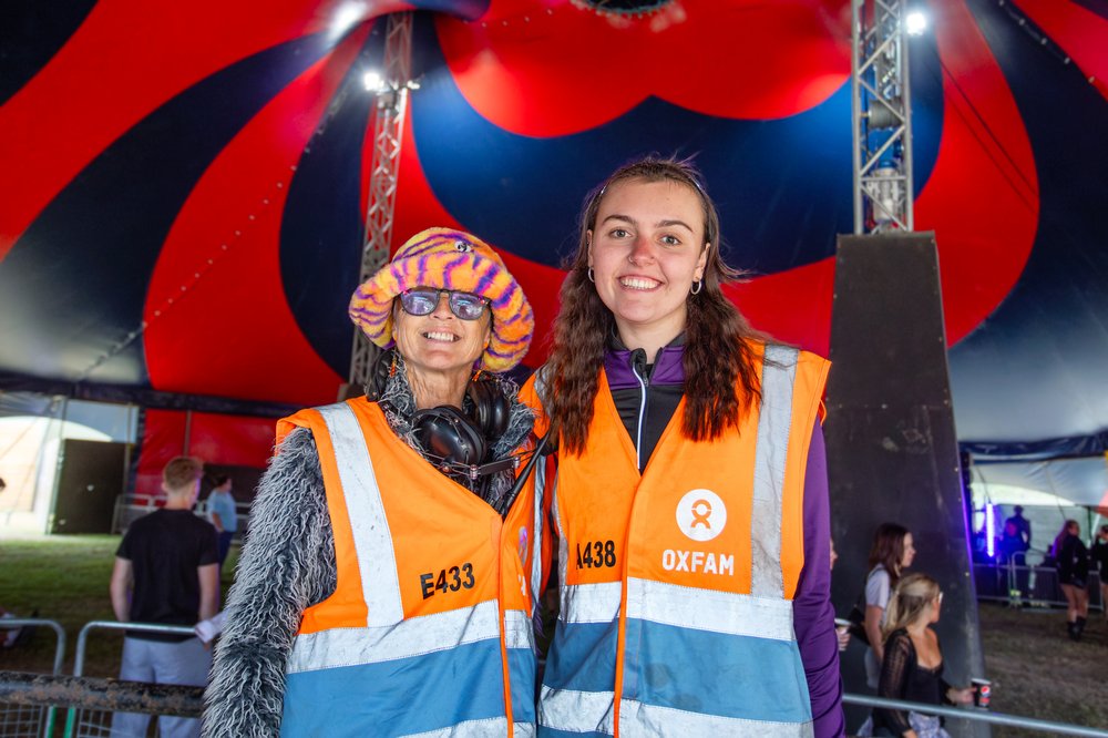 Two smiling Oxfam volunteer stewards posing in a large tent at Leeds Festival