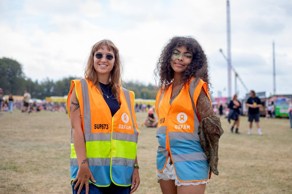 Two smiling Oxfam volunteer stewards posing in the main arena at Leeds Festival