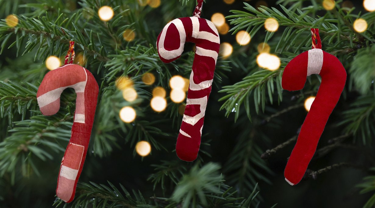 Three handmade red and white candy cane decorations hang on a Christmas tree, surrounded by warm glowing fairy lights.