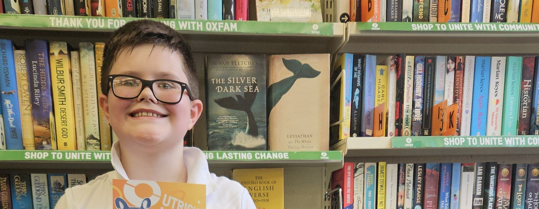 Theo standing beside his upcycled creation, smiling and holding a voucher for Oxfam