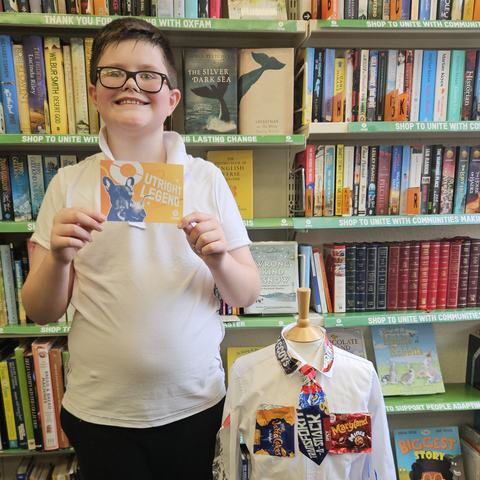 Theo standing beside his upcycled creation, smiling and holding a voucher for Oxfam