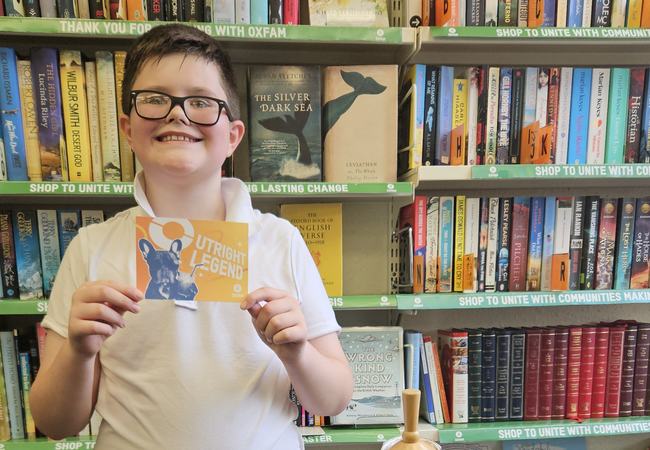 Theo standing beside his upcycled creation, smiling and holding a voucher for Oxfam