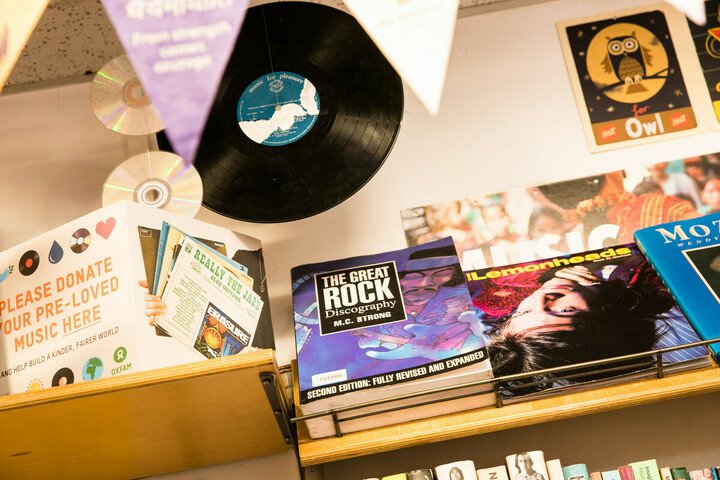 A vinyl, books, cards and bunting atop an Oxfam shop shelf