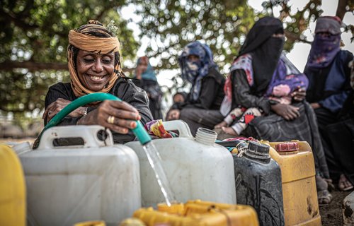 Suad pours water from a hose into a yellow water container