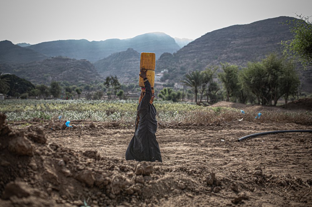 Suad walks past dry mountains with a yellow water container on her head