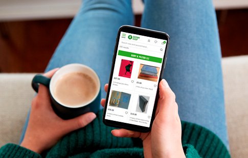 A woman browsing the Oxfam Online Shop on her phone while relaxing with a hot drink.