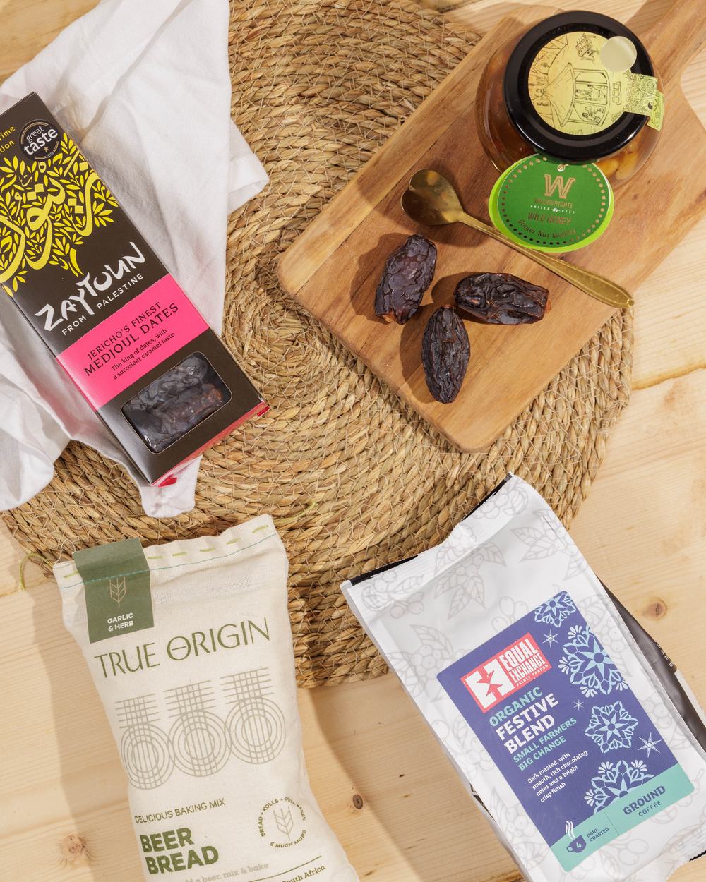 Zaytoun medjoul dates, True Origin Beer Bread and Equal Exchange coffee arranged on a woven placemat and wooden board.