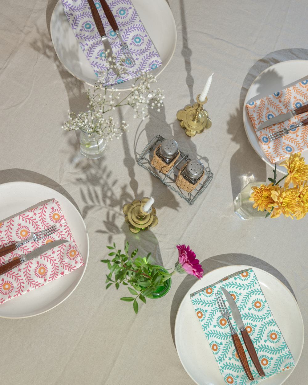 Four white plates with coloured printed napkins and cutlery arranged in a circle on top of a cream blanket.