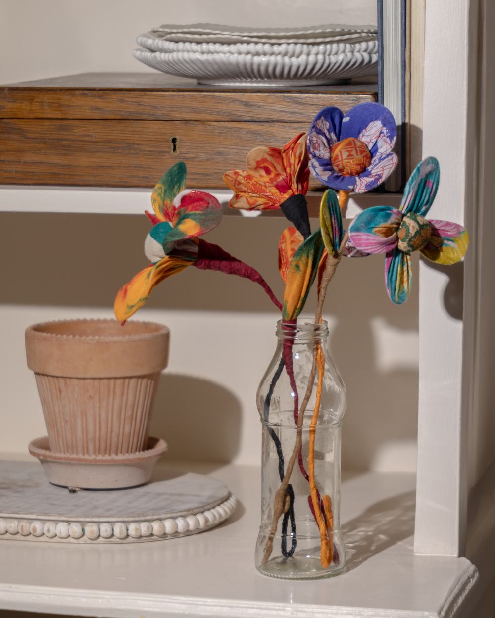 Bouquet of handmade colourful silk flowers in a clear, bottle-shaped vase.