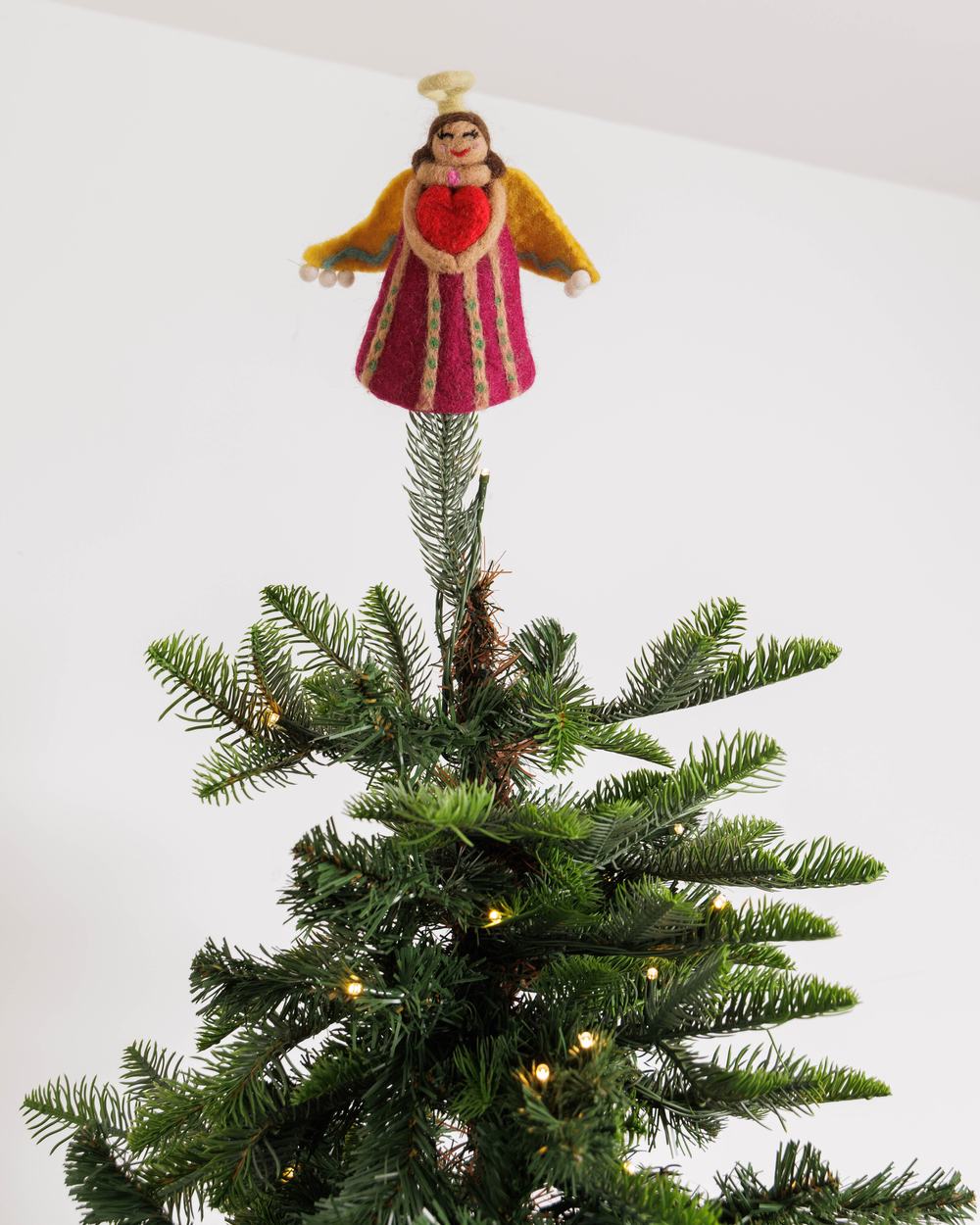 A felt angel decoration on top of a Christmas tree with fairy lights.