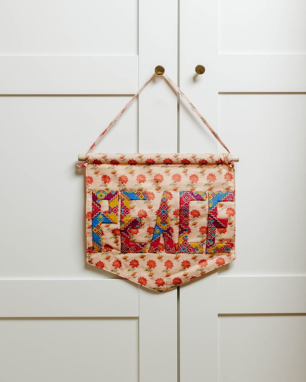 A floral patterned wall hanging made from recycled saris, embroidered with the word 'Peace'.