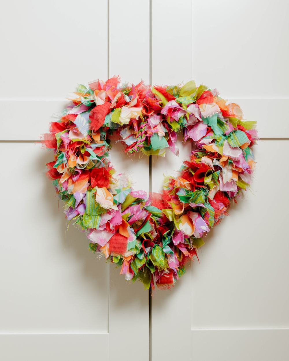 A heart-shaped wreath made from sari fabric, hanging on a door.