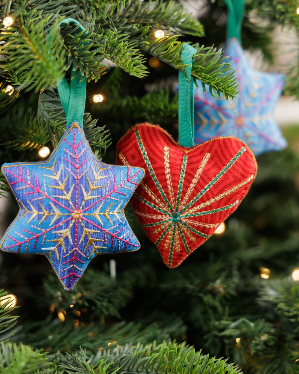 Star and heart Christmas decorations side by side, hanging from a Christmas tree with fairy lights.