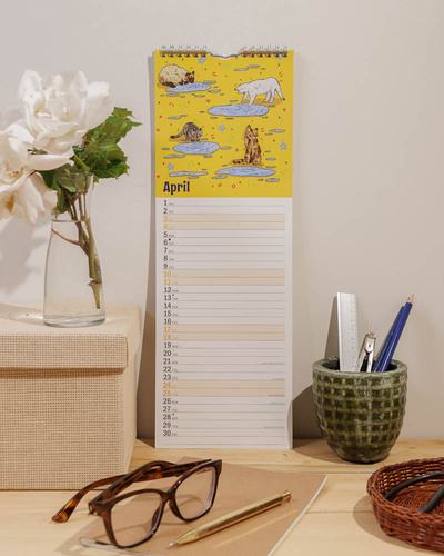 Slim wall calendar with illustrated cats, standing on a desk with office accessories.