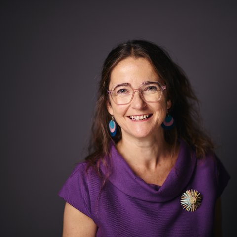Woman with long hair wearing large earrings and a brooch