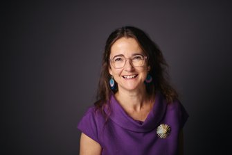 Woman with long hair wearing large earrings and a brooch