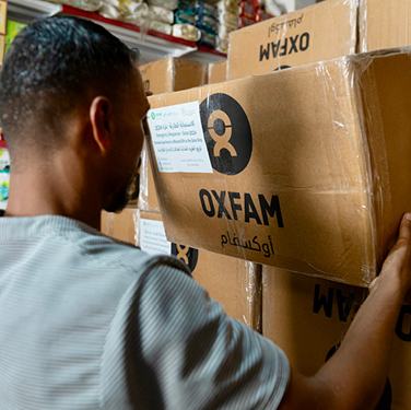 A man lifts a box of aid from a stack of boxes of aid with Oxfam's logo on it