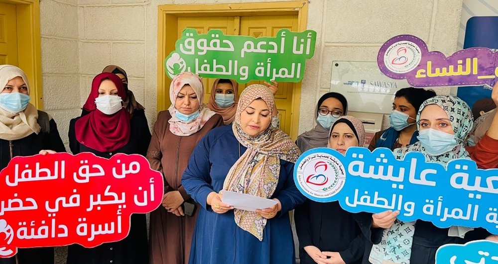 A group of women wearing hijab with red green and blue placards with Arabic text on them.