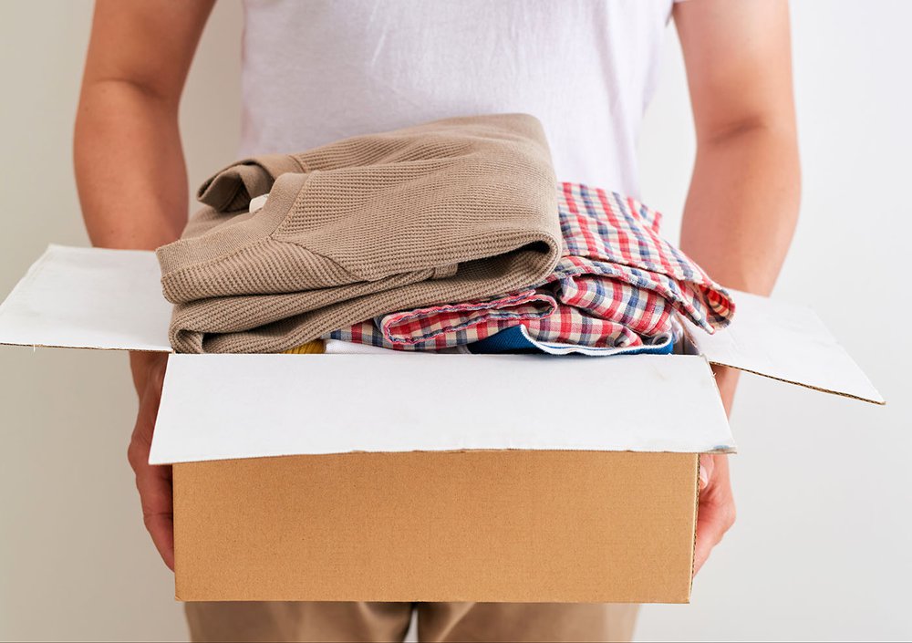 A pair of hands holding a cardboard box full of clothes