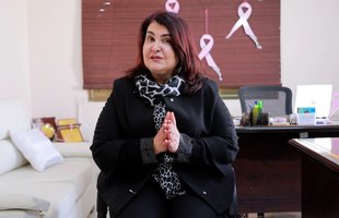 The founder of Aid and Hope with breast cancer pink ribbons on the wall behind her.