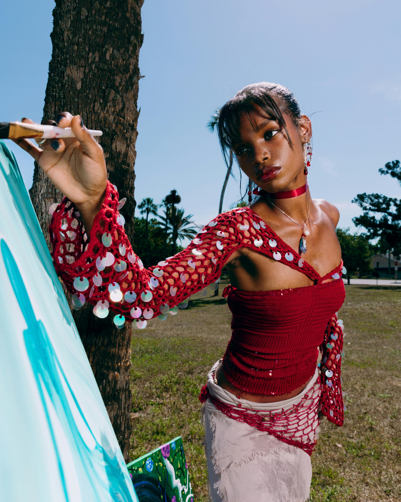 A person wearing a red crochet top and skirt with metallic discs in it with a tropical background.