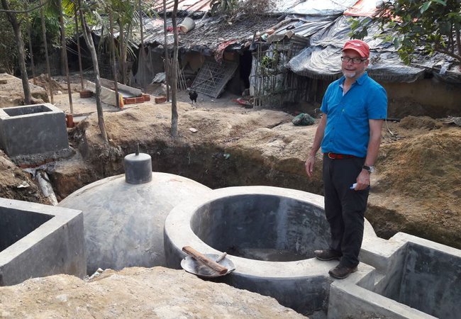 Andy stands by a biogas unit in a refugee camp in Bangladesh