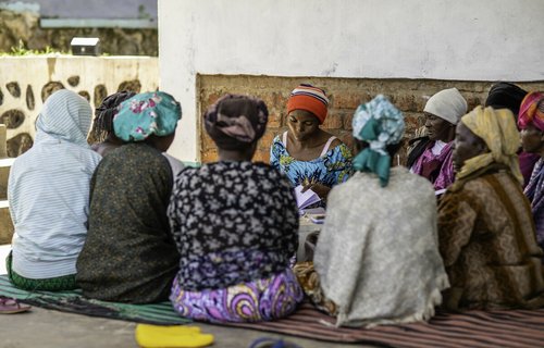 A group of women sit in a circle together, as Murega leads a money collection session.