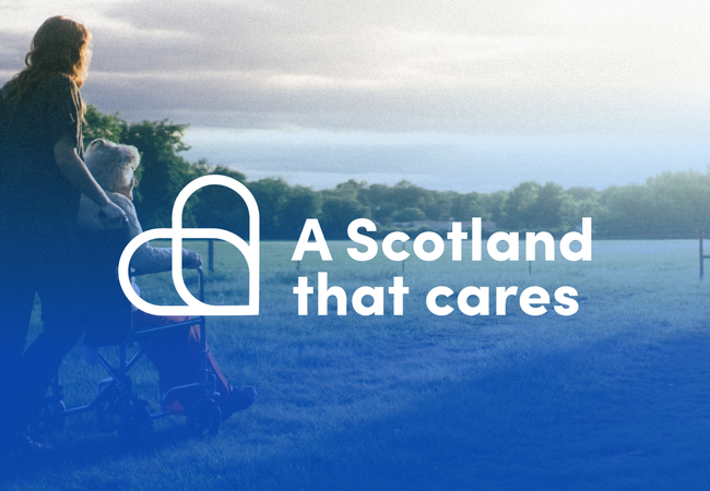 A woman pushing a white haired woman in a wheelchair. Text reads 'A Scotland that cares'