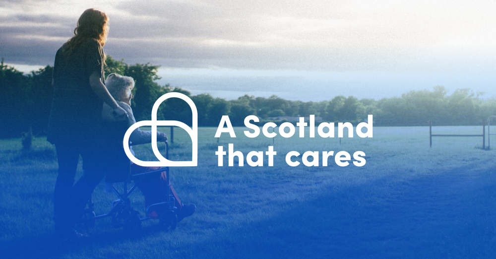 A woman pushing a white haired woman in a wheelchair. Text reads 'A Scotland that cares'