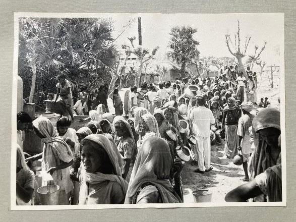 An old black and white photo of a large group of people holding empty containers, gathering in a street in Bihar, India.