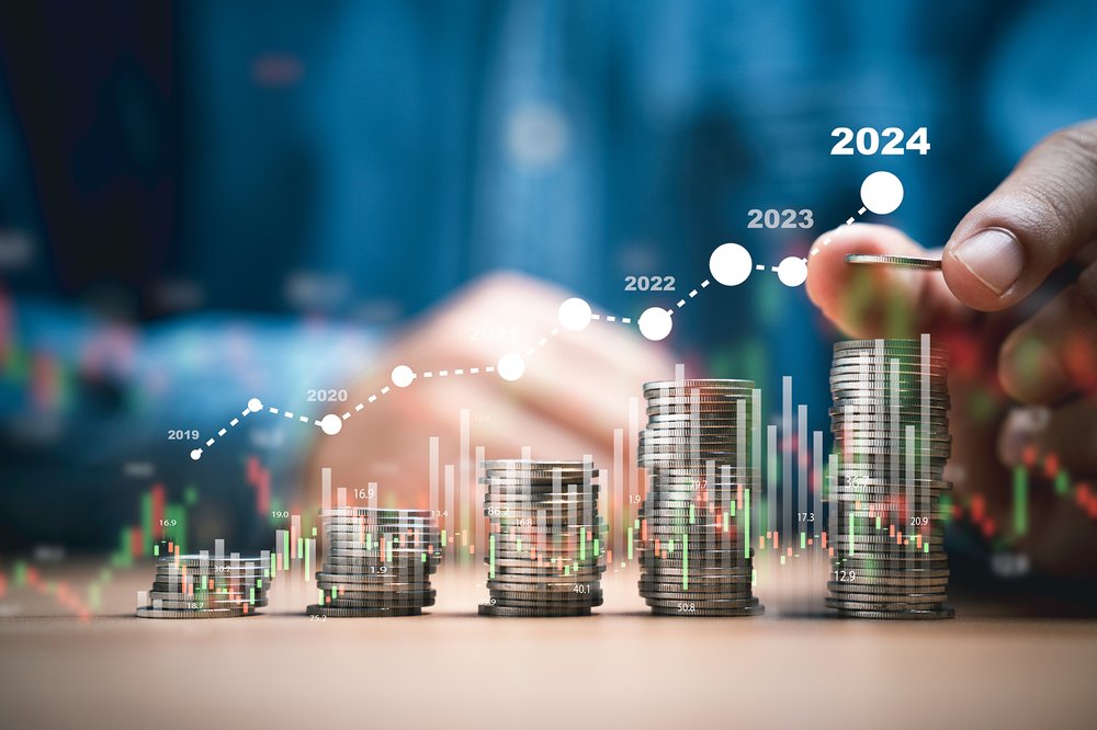 Five stacks of coins are arranged in ascending height, each labelled with a year, starting from 2019 to 2024. A hand is in the process of adding to the 2024 stack, symbolising growth or accumulation over time.