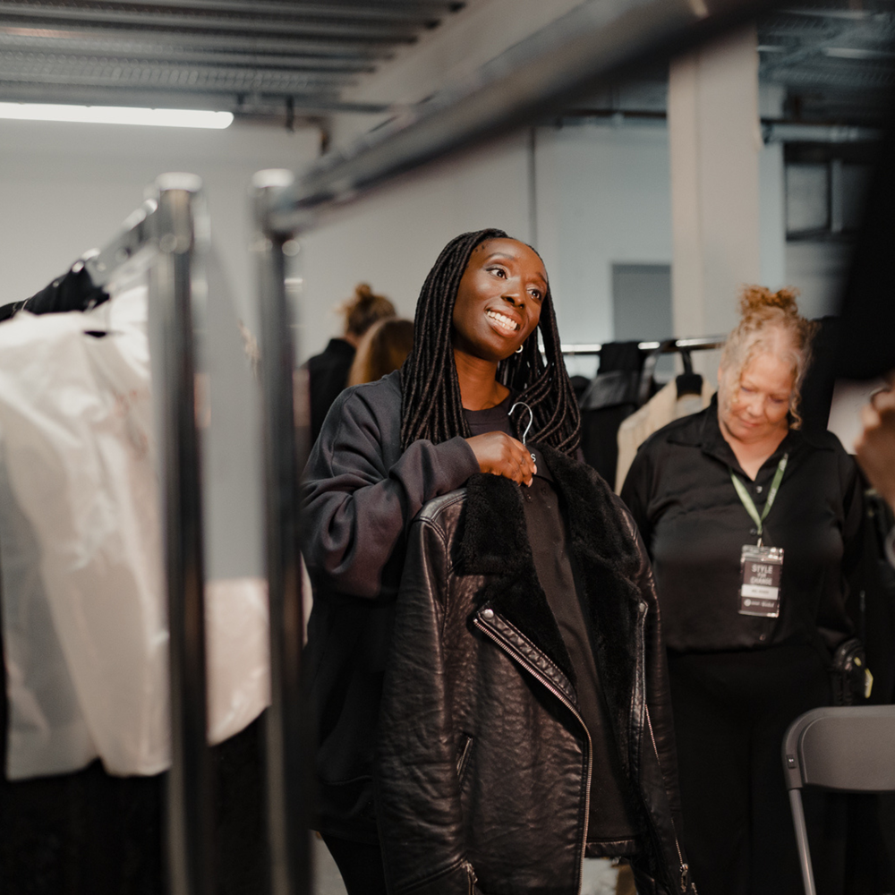 Eunice Olumide holding up a black jacket backstage, smiling before the show.
