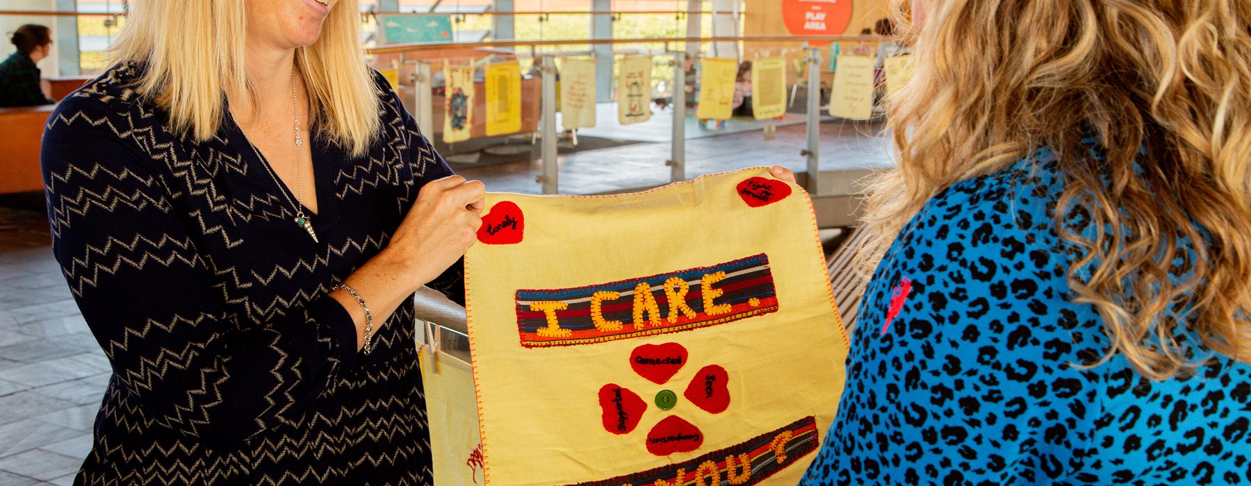 A smiling woman holds up an embroidery reading 'I care, do you?'
