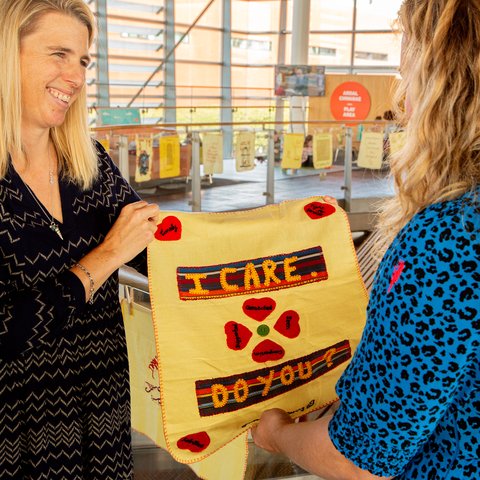 A smiling woman holds up an embroidery reading 'I care, do you?'