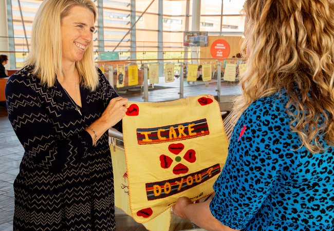 A smiling woman holds up an embroidery reading 'I care, do you?'
