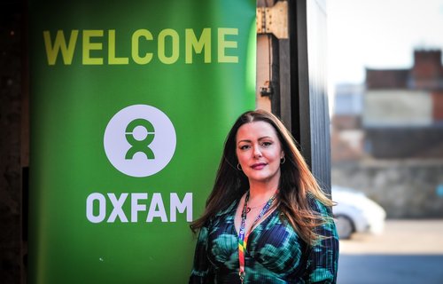Corrine Jones from Oxfam's in-memory team stands in front of a banner with the Oxfam logo reading 'Welcome'.