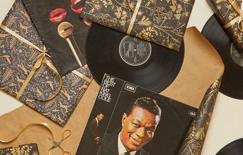 A selection of vintage vinyl records, including albums by Diana Ross and Nat King Cole, displayed among gold-patterned Christmas gift wrap, ribbons and wrapped presents.