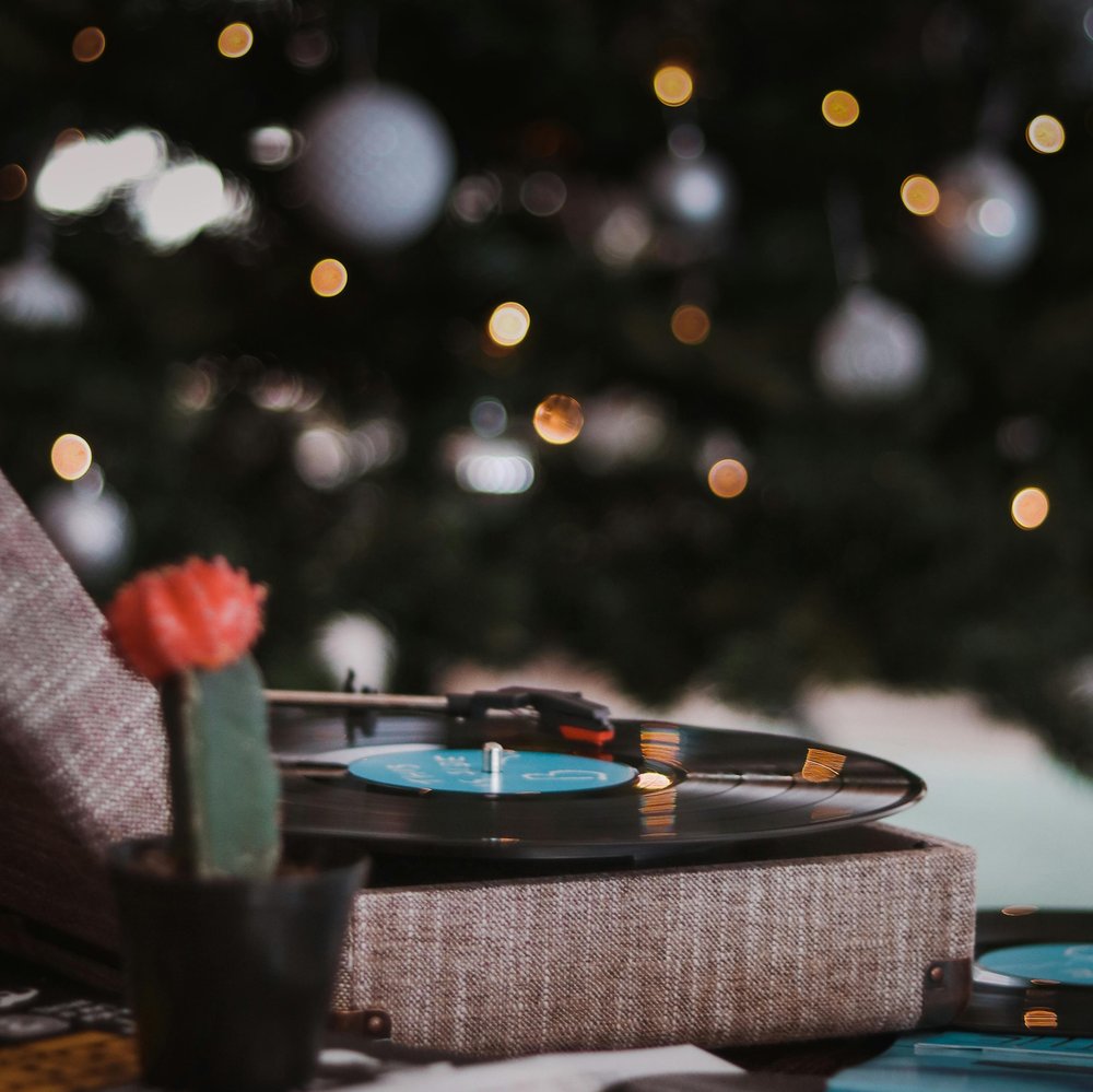 A festive setting with a blurred tree with yellow lights in the back, in focus you can see a record player open with a vinyl playing.