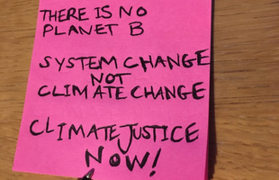 A pink post-it pad with three messages: there is no planet b, system change not climate change and climate justice now written on the top post-it