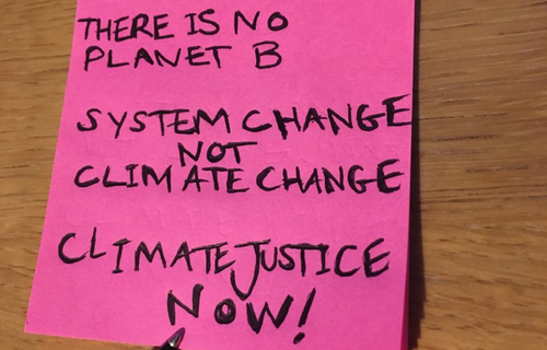 A pink post-it pad with three messages: there is no planet b, system change not climate change and climate justice now written on the top post-it