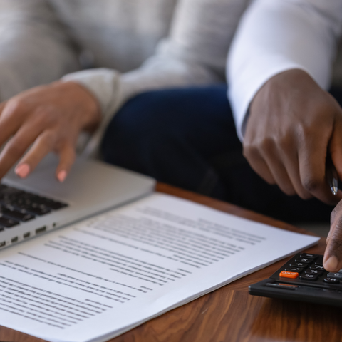 The hands of a man and a woman doing their finances with a calculator, computer and some papers.